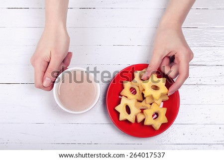 Women\'s hands with a cup. Cup of cocoa and cookies on the table. White wooden table, cup, saucer, pastries and female hands. Cup on the table. Girl drinking hot chocolate. Coffee shop, restaurant.