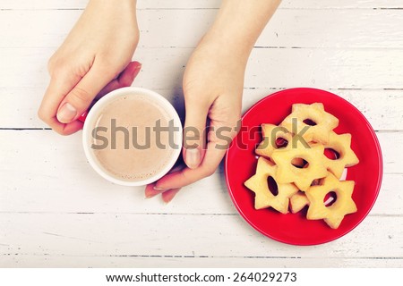 Women\'s hands with a cup. Cup of cocoa and cookies on the table. Cup on the table. Girl drinking hot chocolate. Snack, coffee shop, restaurant.  White wooden table, cup, saucer, pastries and hands.