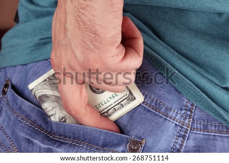 A man with money. Hiding money in the back pocket of his jeans. A man in a t-shirt and jeans hides the money in his pocket. Hairy male arm. The wad of money in hand.