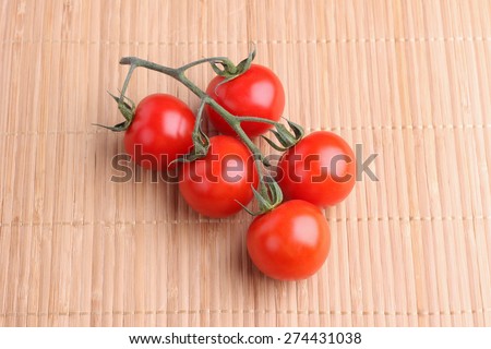 Red tomatoes on a branch. The cherry tomatoes. Branch of tomatoes on the table. Straw napkin on the table and vegetables. Ripe tomatoes. Juicy vegetables. Berry.