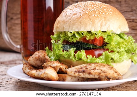 Glass of dark beer and Burger meat. Lettuce, cucumber, tomato, bread, meat and beer. An alcoholic drink. A plate with meat and Burger. Fried chicken meat. Food and Beer. Meat and beer.