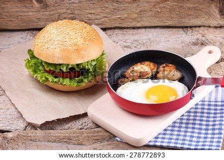 The pan with fried egg and meat. Burger with vegetables. Sandwich with lettuce, tomato and cucumber. White fresh bread, and vegetables. Rich breakfast.