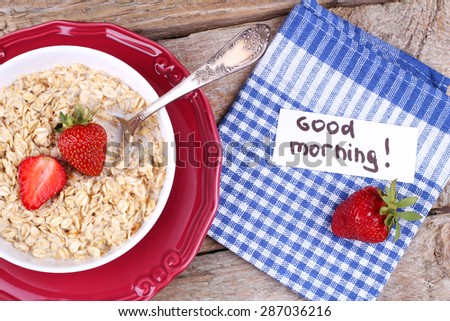 Oatmeal with strawberries. Ripe strawberries, oatmeal with milk and a note. Good morning. Surprise, the wish. Note the banner. Healthy food, diet. Delicious and healthy Breakfast. Portion of oatmeal.
