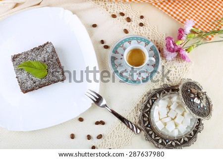 Chocolate brownie on a plate. Dessert on a platter. Cup of ristretto, dessert and sugar bowl. Espresso, sugar bowl and cake. Carnation flowers and food on the table. A coffee shop, restaurant.
