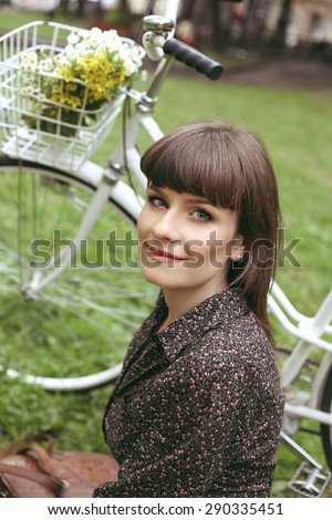 Girl and retro bike. City bike and beautiful girl. Romantic girl with flowers and a Bicycle. Bicycle, basket, flowers. A mysterious look. Beautiful young woman sitting on the lawn. Retro look.