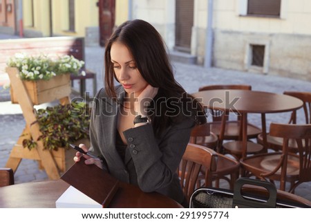 Beautiful confident woman. Woman on the street at the table . Business woman outdoors. Business consultant, to note down, to make notes. Woman in cafe. Business style. Outdoor cafe. Woman in cafe.