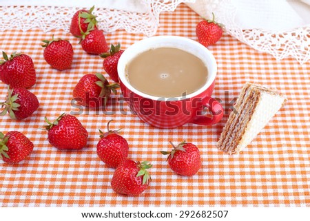 The kitchen table with a cup of coffee, dessert and strawberries. Strawberry berry, waffle cake and a cup of hot coffee with milk. Summer berries. Breakfast, snack, food.