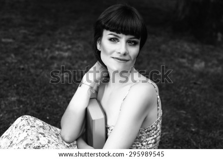 Girl with the book. Hugging the book. Portrait of a beautiful girl. Woman\'s portrait. Relax in the Park. Girl in sundress on the street. Black and white photo. Woman with book.