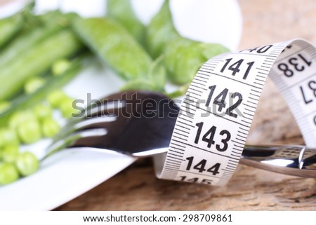 Fork on a white plate. Fork with measuring tape on the table. Wooden table, fork, plate and measuring tape. Food, peas, and vegetables. Pea pods. Diet, diet food. Fork and food.