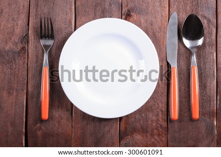 White plate on the table. Empty plate. Fork, knife and spoon on the table. Laying the table. Starvation diet. Template, background, space for text. Restaurant, catering, cafeteria. For food.