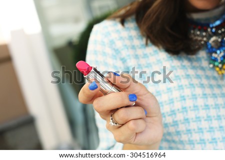 Bright pink lipstick in the hands of the girl. Lipstick in her hands. Cosmetics. Stylish girl in a dress and necklace. Necklace with rhinestones. Brown-haired woman with lipstick. Lipstick.