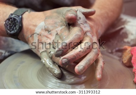 Men\'s hands. Potter at work. Creating dishes. Potter\'s wheel. Dirty hands in the clay and the potter\'s wheel with the product. Creation. Working potter. Centering clay. Selective focus.