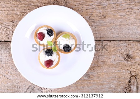 Plate with cakes on an old table. Three cream cake with berries. Berry dessert. Sweet table. Sweet food. White plate with a cakes. Blackberry, raspberry and mint leaf.