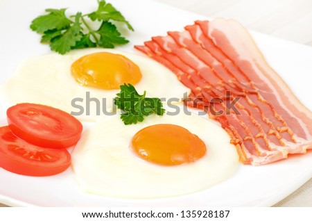 Breakfast with fried eggs, bacon and slices tomatoes