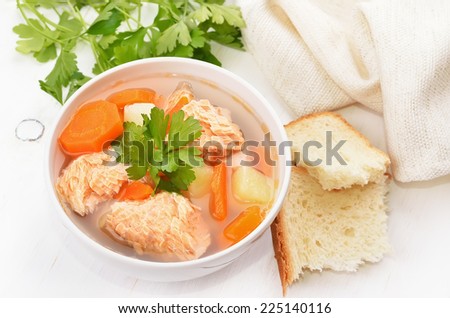Fish soup with salmon in bowl and bread on white wooden table