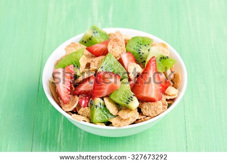 Corn flakes with fresh strawberry and kiwi slices in bowl on green table