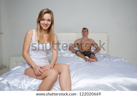 Young woman smiling in bedroom, man lying on bed