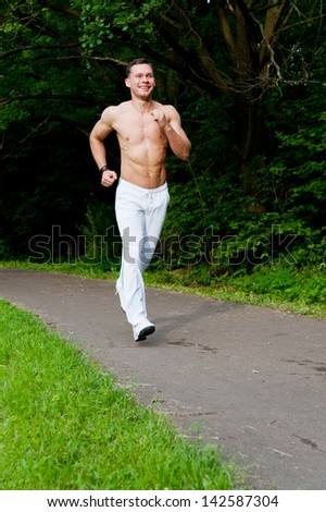 Man in white pants runs on the road in the park