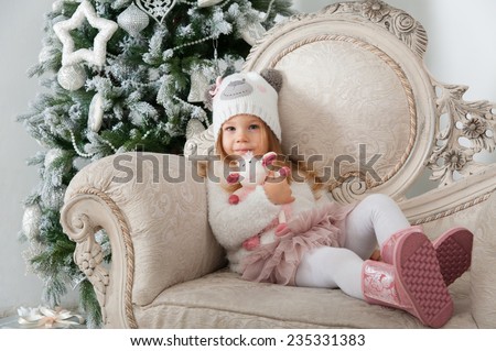 Child girl in bear hat with sheep toy sitting on background of Christmas tree, Happy New Year theme