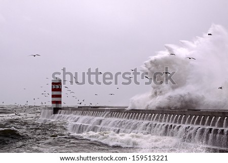 Moody seascape with big wave, pier, lighthouse and seagulls flying over crashing wave