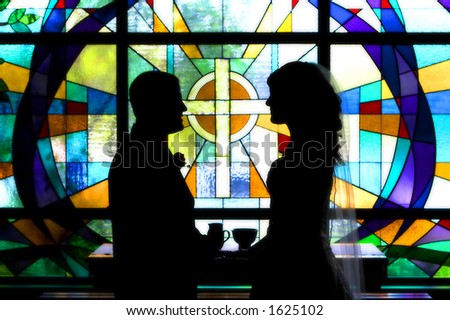 Bride and groom holding hands in front of a stained glass window with a cross on it.