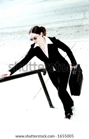 Young woman in business attire, carrying briefcase and walking up some steps.