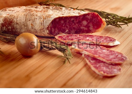 Sliced dried french sausages with rosemary and olive on wooden table