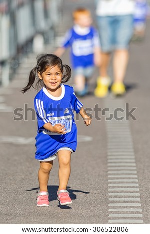 STOCKHOLM, SWEDEN - AUGUST 15, 2015: Young happy girl with big blue shirt running the Minimil for the youngest runners at Midnattsloppet. The track is 300 meters and the runners are aged 2-8 years.