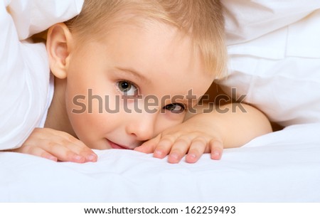 child little boy is lying in bed under a white blanket