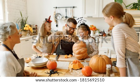 Happy multi generational family smiling and carving jack o lantern from pumpkin while gathering around table during Halloween celebration