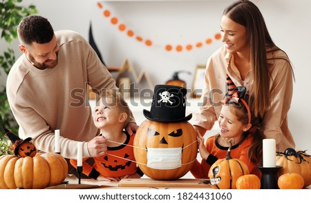 Cheerful family   makes jack o lantern  in medical masks out of a pumpkin and  decorates house  in cozy kitchen during Halloween celebration at home during the covid19 coronavirus pandemic