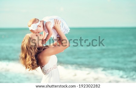 happy familyin white dress. Mother throws up  baby in the sky in beach