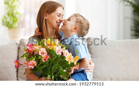 Optimistic family: mother with bouquet of  alstroemeria laughing and touching nose with happy son  during holiday celebration  mothers day at home
