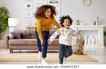 Playful african american mother trying to catch excited small child son while playing together at home, playful mom and kid running and having fun in living room. Happy family enjoying leisure time