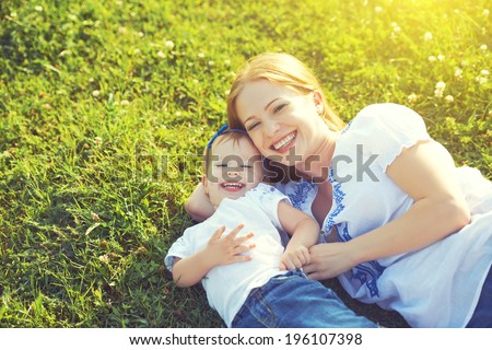 happy family on nature. mom and baby daughter lying are playing and laughing in the green grass