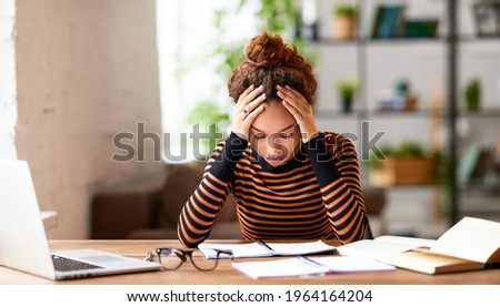 Stressed young afro american woman holding head in hands and feeling demotivated while sitting at her home office and working remotely on laptop. Depressed female student tired of onling learning Foto d'archivio © 