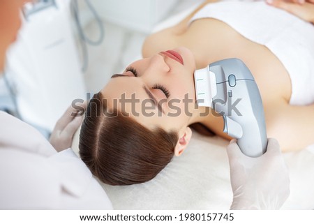 From above of relaxed young female client getting SMAS ultrasound face lifting massage with professional equipment in beauty center