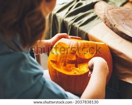 Cropped shot of female carving large orange pumpkin for Halloween party while sitting at wooden table at home, making scary face on jack-o-lantern with knife to set the mood for trick-or-treaters Foto stock © 