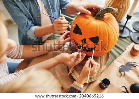 Cropped shot of family parent with little kids preparing for holiday Halloween, hands of mother with children drawing scary face with paint brushes together on pumpkin for house decoration Foto stock © 
