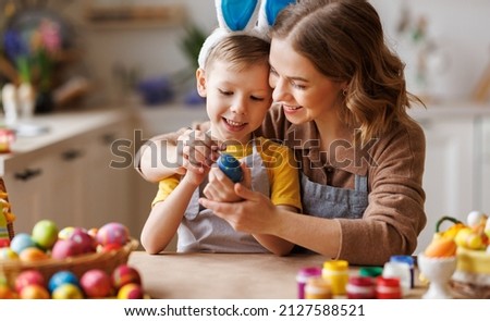 Easter Family traditions. Loving young mother teaching happy little kid soon to dye and decorate eggs with paints for Easter holidays while sitting together at kitchen table, selective focus Stock foto © 