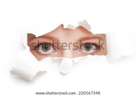 eyes of a young curious woman peeking through a  hole torn in white paper poster
