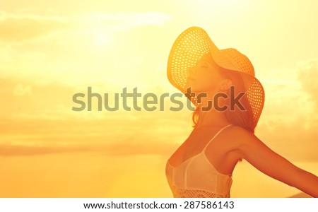 Happy beauty woman in a hat opened his hands, relaxes and enjoys the sunset over the sea on the beach