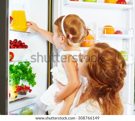 happy family mother and baby daughter drinking orange juice in the kitchen near the refrigerator
