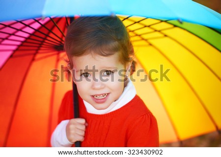 Beautiful little child girl with multicolored rainbow umbrella on nature in the park