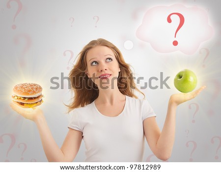 attractive girl makes a choice between healthy and unhealthy foods, apple and hamburger on a modern conceptual background