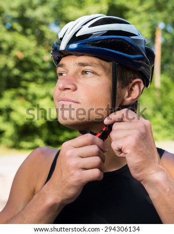 Serious professional cyclists wear a helmet for his safety and buttons on the helmet buckle under the neck. Bicycle helmet blue with white, in the morning in the green forest.