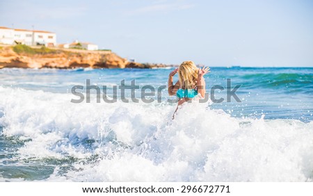 beautiful young blonde woman jumping in big waves in the blue sea bright day in the resort in Europe