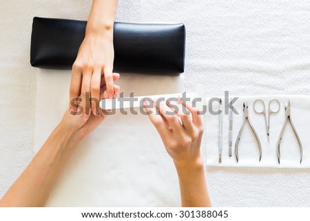 Beautician filing a clients nails as she performs a manicure in the salon, overhead view of their hands and laid out beauty tools