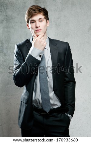 Young businessman in gray suit thinking or dreaming, on gray background