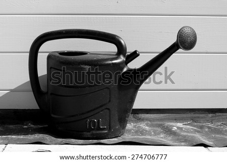 Black and white plastic watering can in the sun parallel to wooden panels of summer house or garden shed